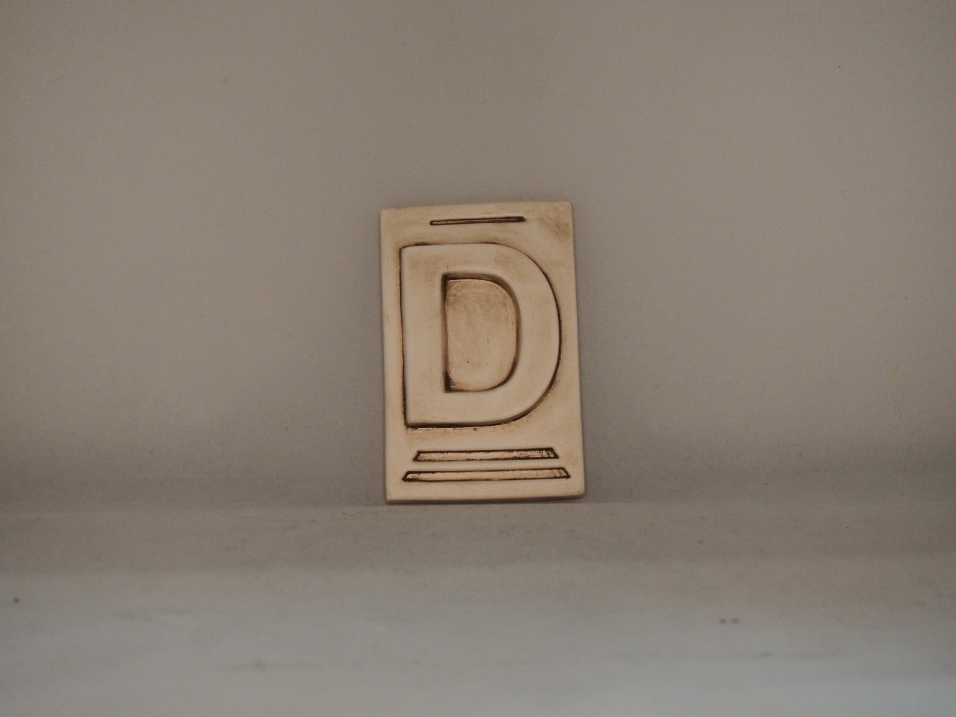 Placa decorativa de madeira com a letra D gravada em bege