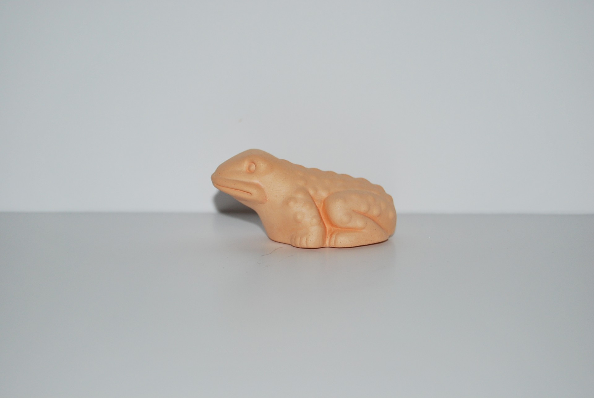 Figura de rã laranja em plástico com textura rugosa sobre fundo branco