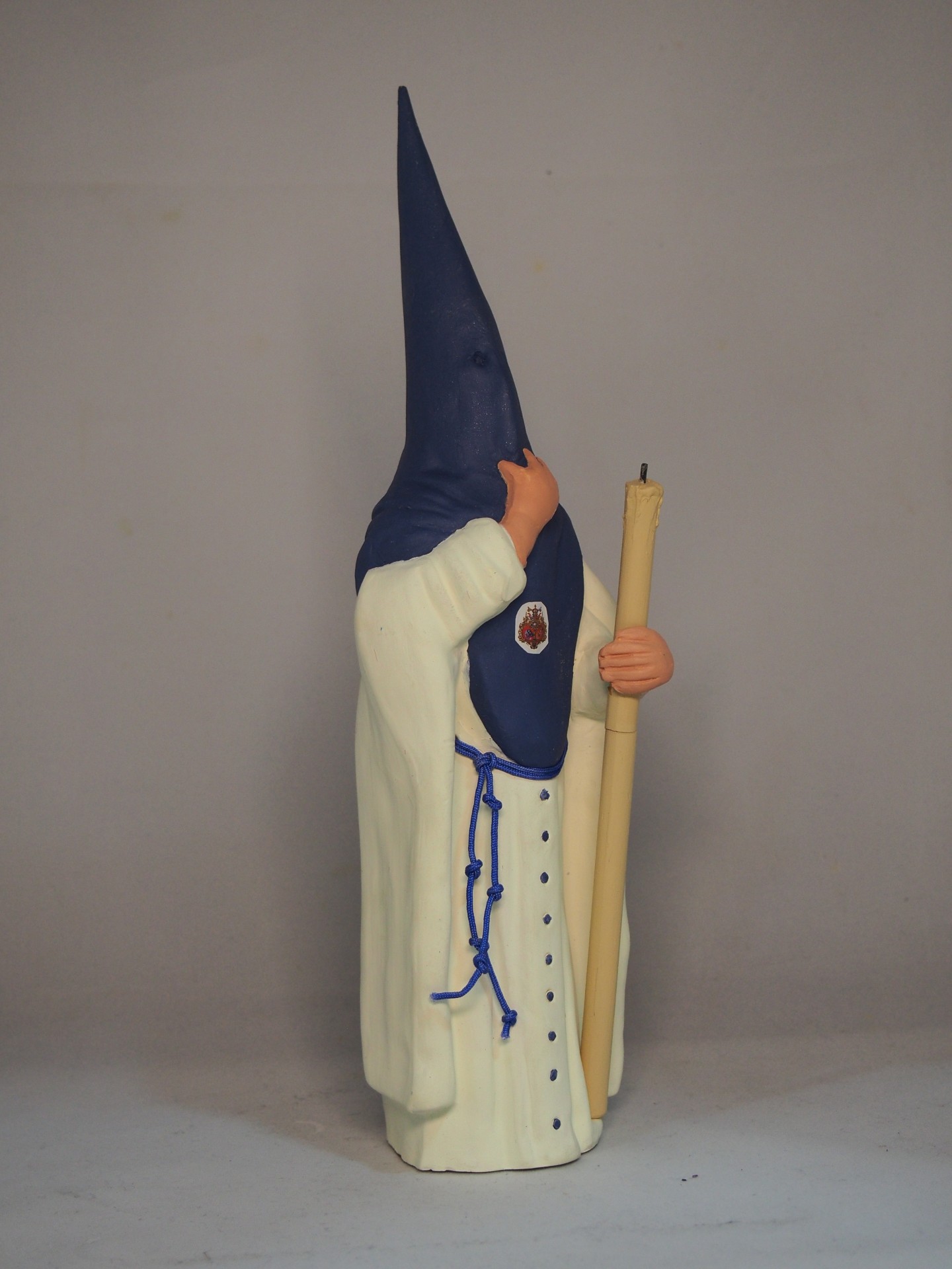 Estatueta religiosa em túnica branca e capuz azul segurando vela amarela