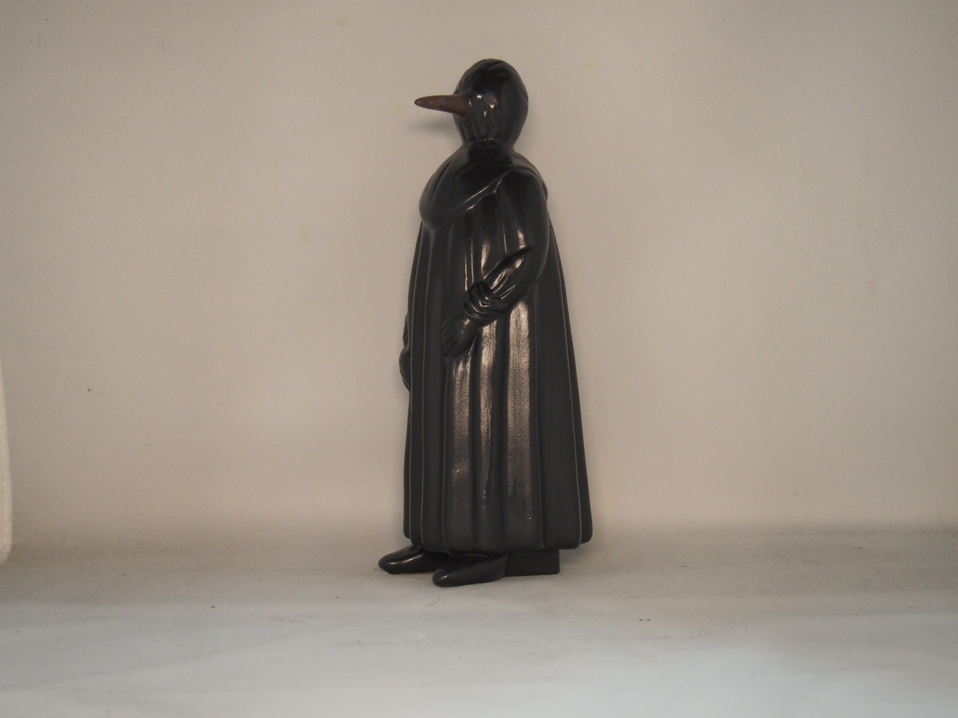 Figura decorativa preta em forma de pássaro com corpo humano e capa longa