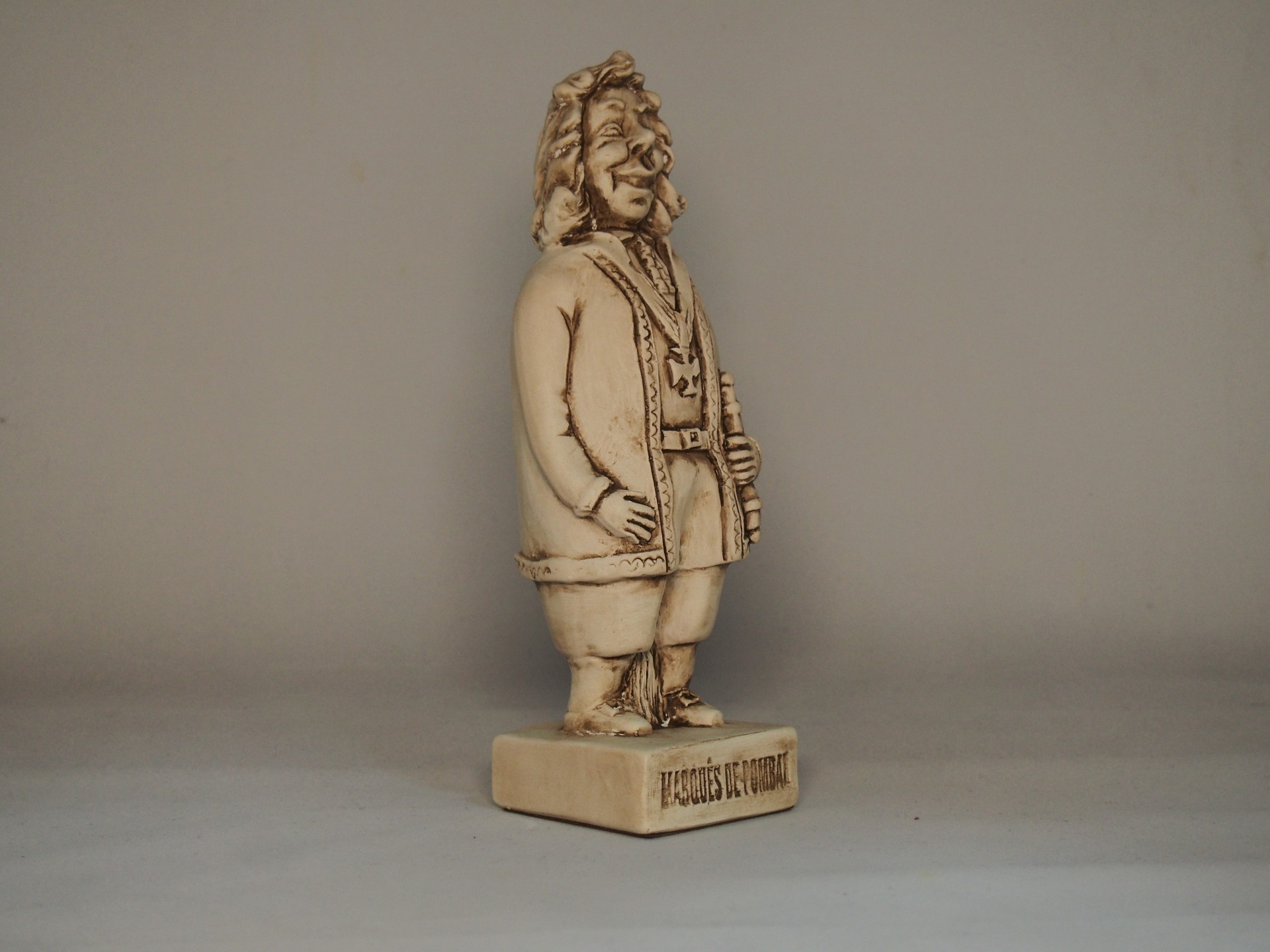 Estátua bege clara de homem com cabelos encaracolados, casaco e botas, base com inscrição PEDRO II IMPERADOR