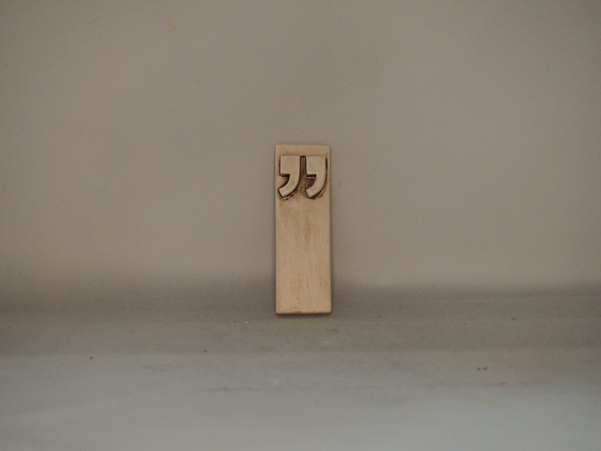 Marcador de páginas de madeira clara com aspas em relevo