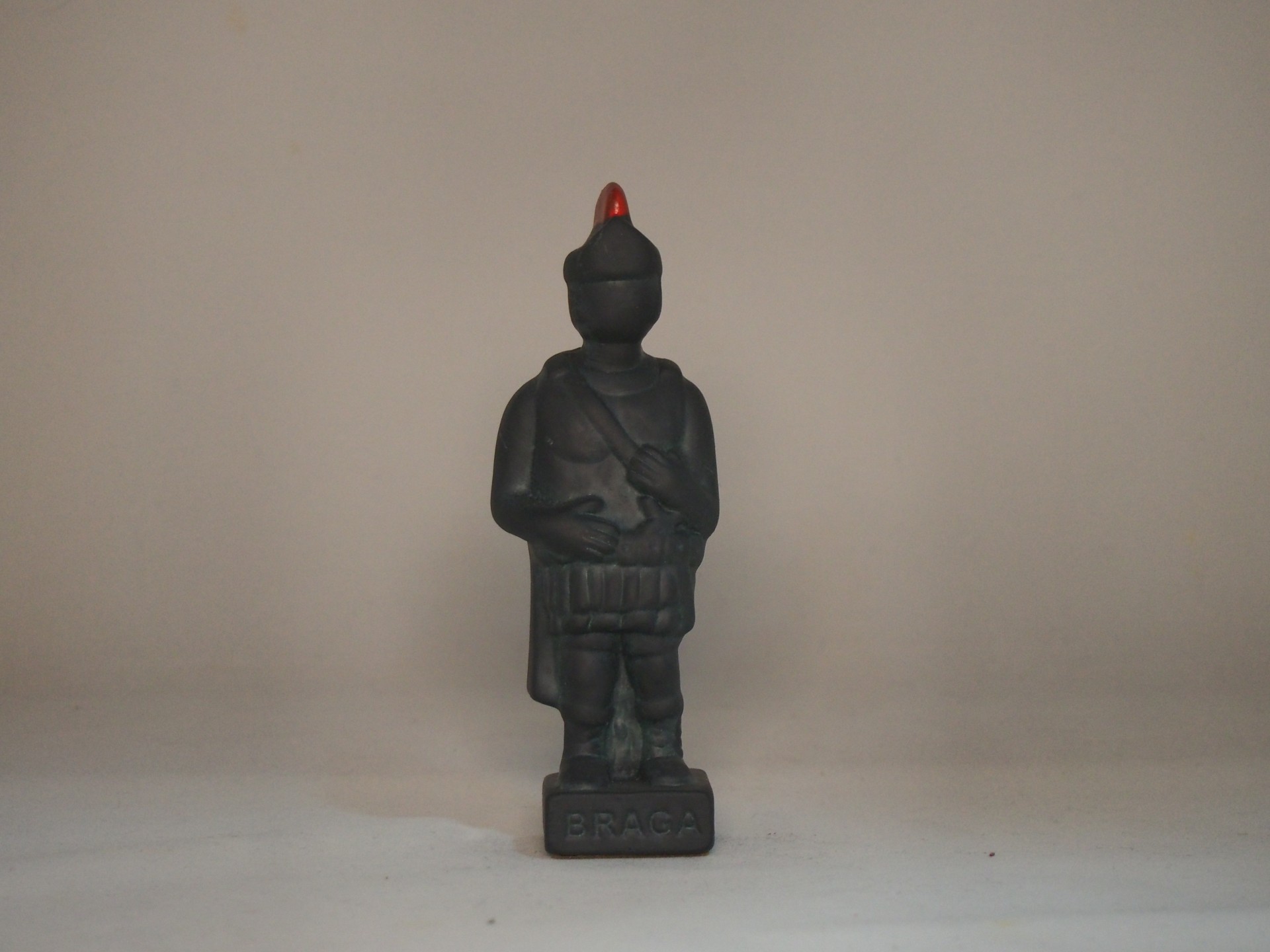 Figurina preta de soldado com chapéu vermelho em base com texto B.P.A.G.A.