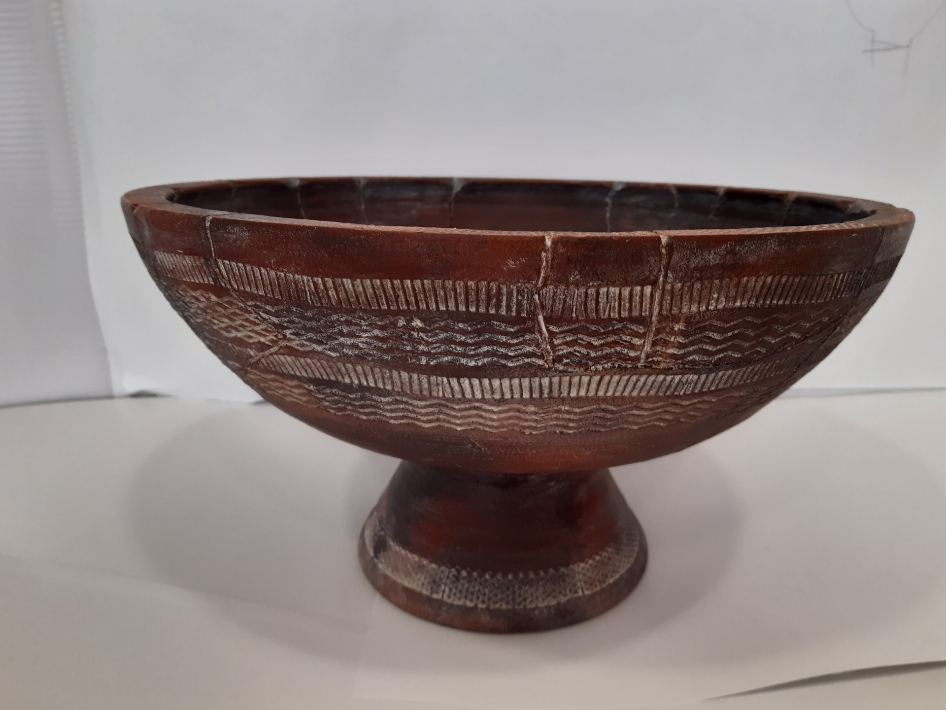 Tigela de cerâmica castanha com padrões entalhados brancos sobre base elevada