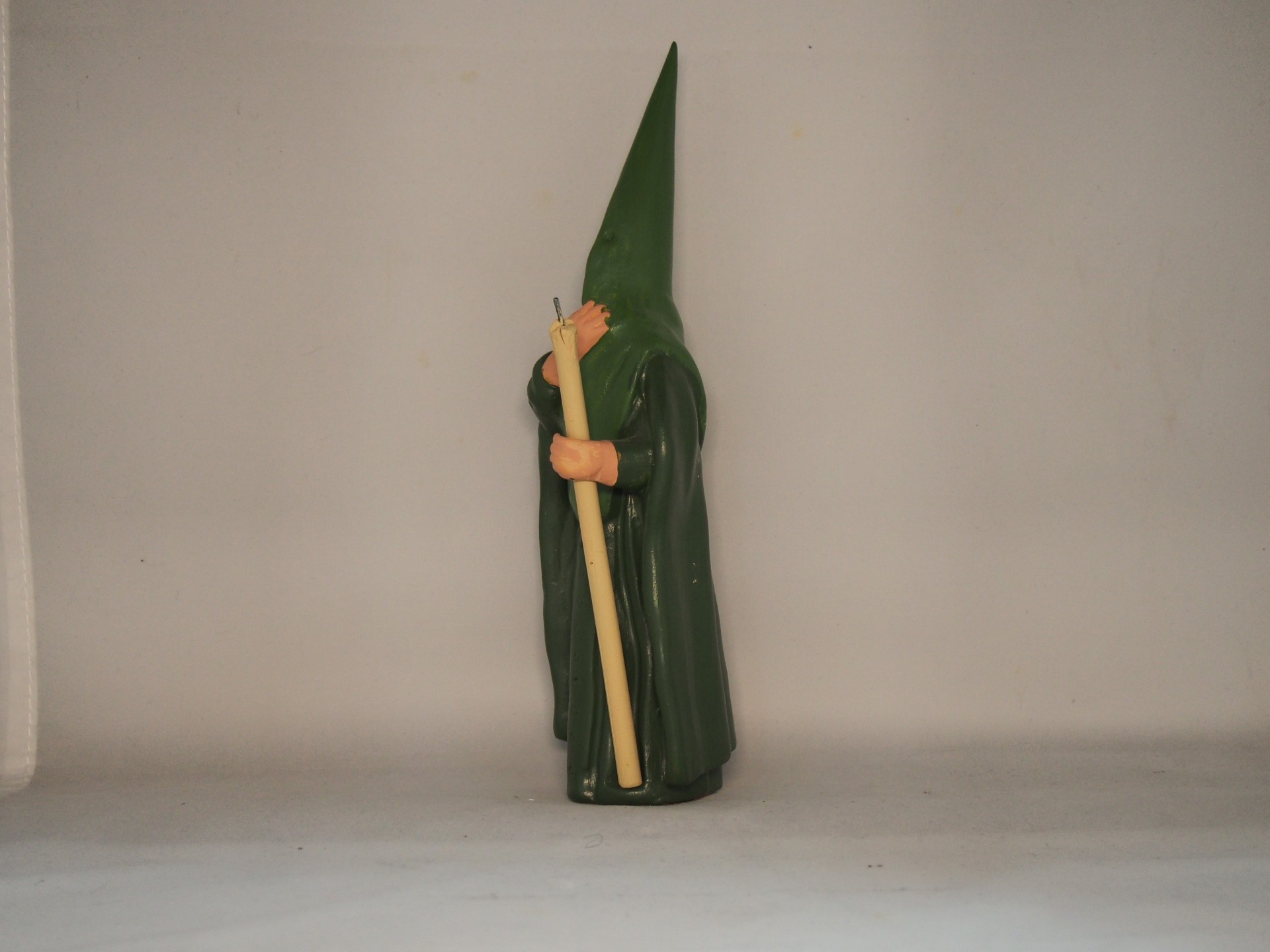 Figura decorativa com túnica verde e capuz pontiagudo segurando um objeto longo