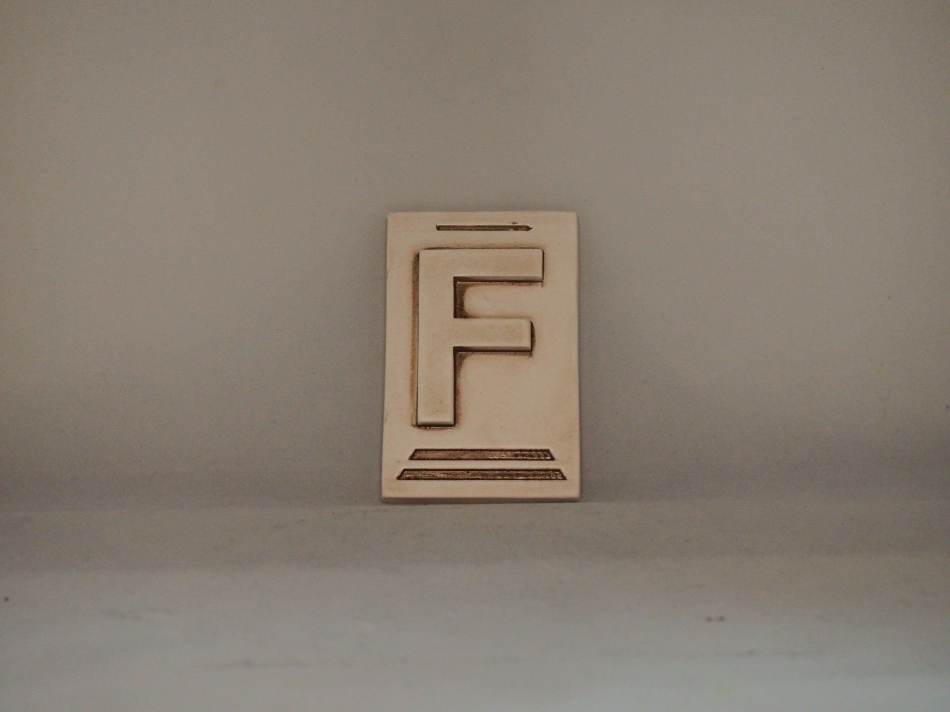 Placa de madeira clara com a letra F em relevo