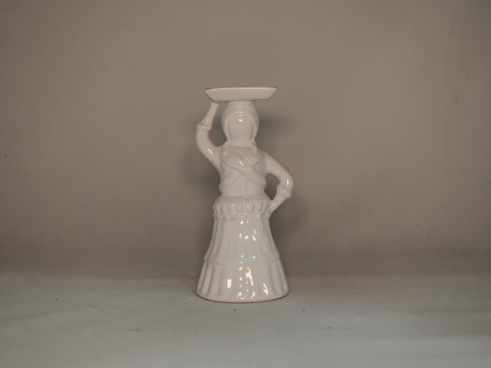 Estatueta branca de cerâmica com mulher e prato na cabeça