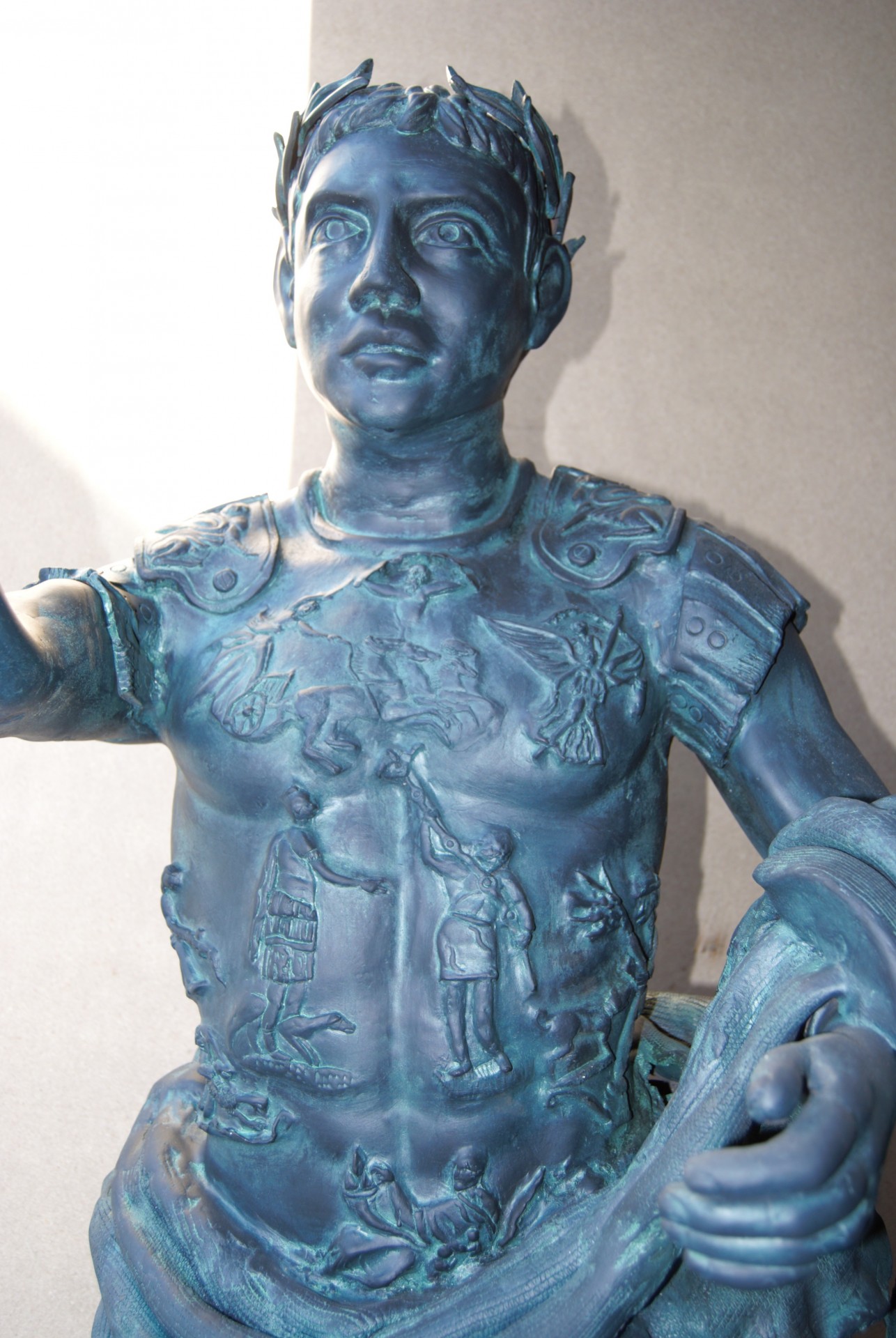 Estátua azul esverdeada de guerreiro romano com armadura detalhada e coroa de folhas