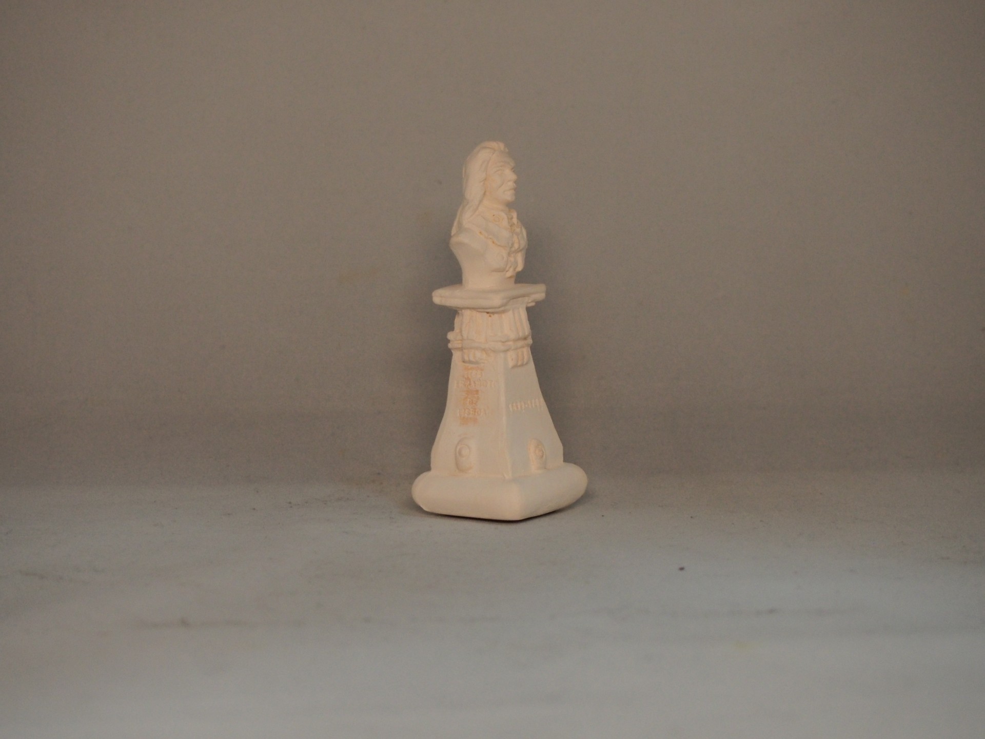 Peça decorativa branca com busto em pedestal sobre fundo cinzento