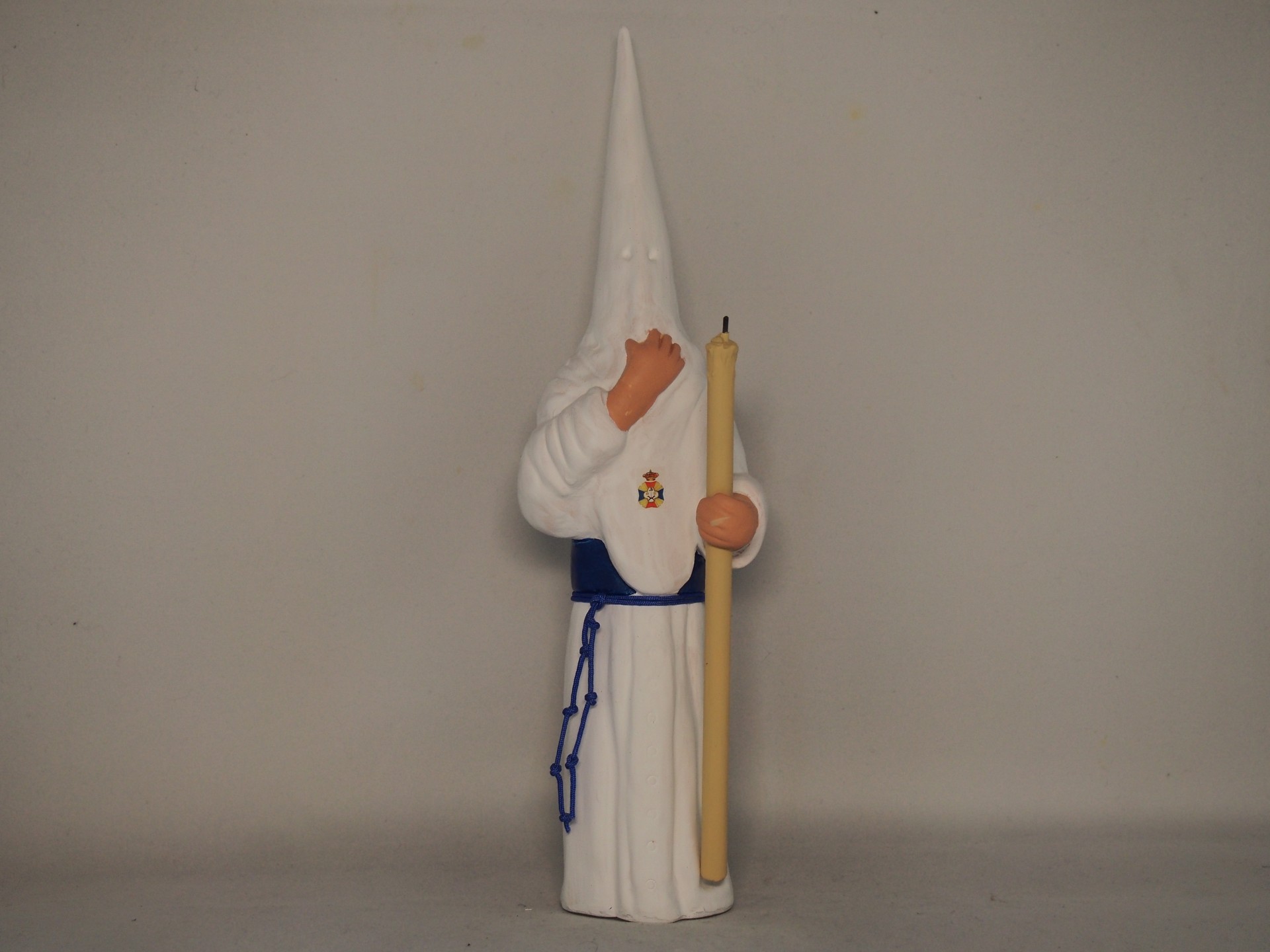 Boneco figurativo com capuz branco e faixa azul segurando objeto amarelo