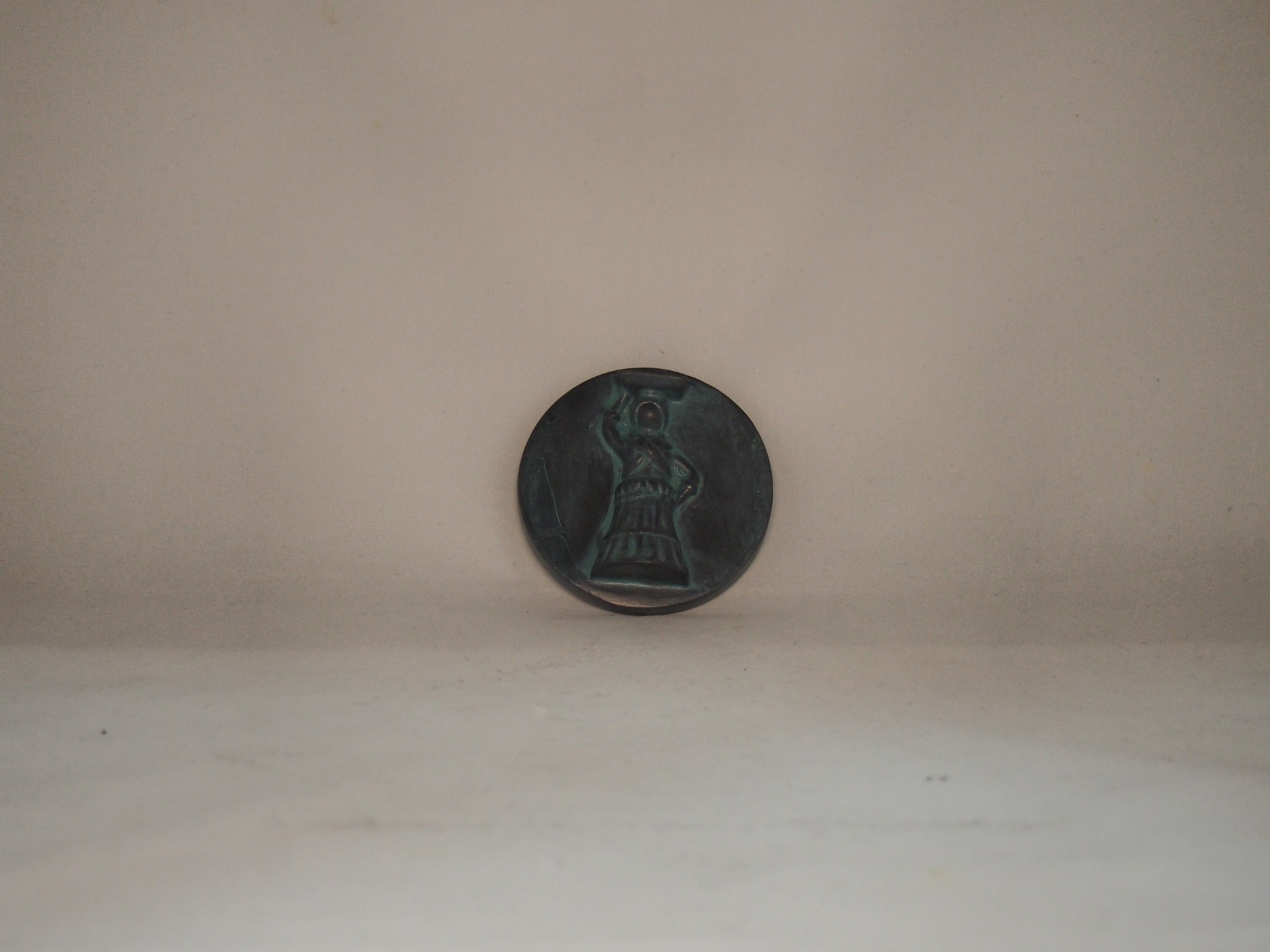 Botão redondo em metal escuro com relevo de figura humana