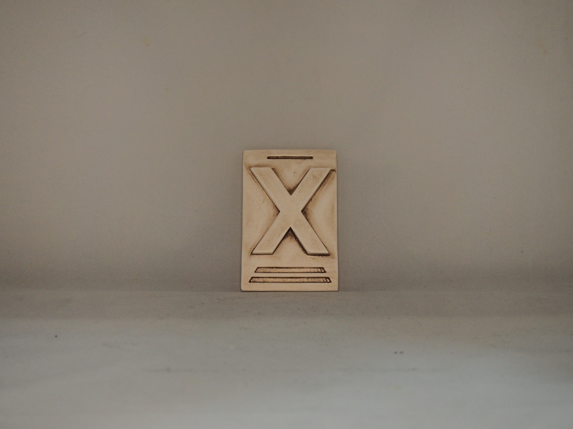 Bloco de madeira com um X gravado em relevo colocado numa superfície cinzenta