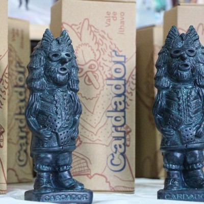 Duas estatuetas escuras de lobo antropomórfico com caixas ao fundo da marca Candador