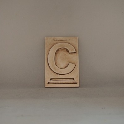 Placa decorativa bege com a letra 'C' em relevo