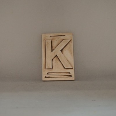 Placa decorativa bege com letra K em relevo