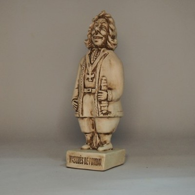 Estátua bege claro de figura masculina com túnica, segurando objeto, sobre base com texto