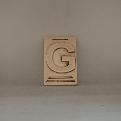 Peça decorativa bege com relevo da letra G