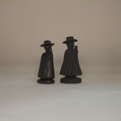 Duas miniaturas pretas de figuras humanas com capa e chapéu