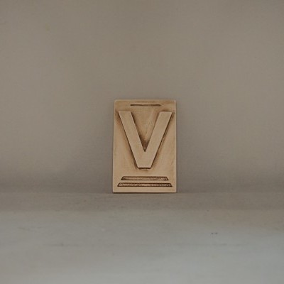 objeto decorativo em madeira clara com letra V em relevo