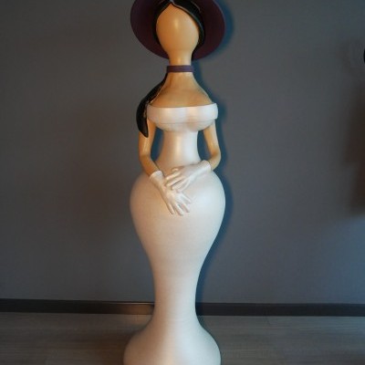 Estátua decorativa de mulher estilizada, vestido creme, chapéu roxo, em fundo cinza