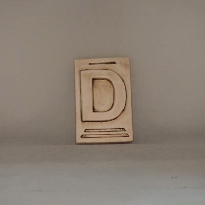 Placa decorativa de madeira com a letra D gravada em bege