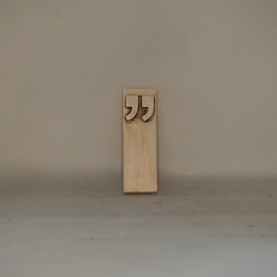 Marcador de páginas de madeira clara com aspas em relevo