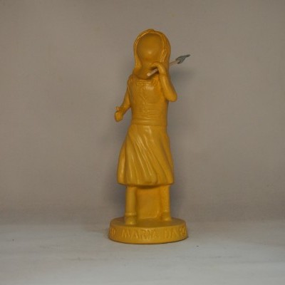 Estatueta amarela de menina com vestido e chapéu em fundo cinza