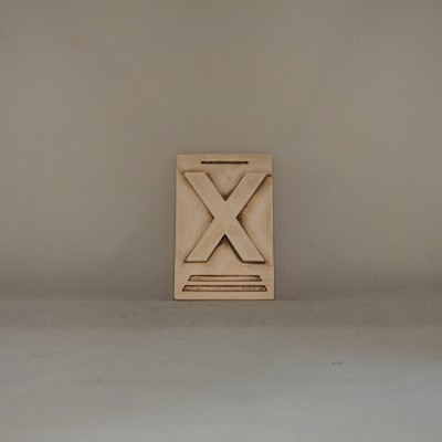 Bloco de madeira com um X gravado em relevo colocado numa superfície cinzenta