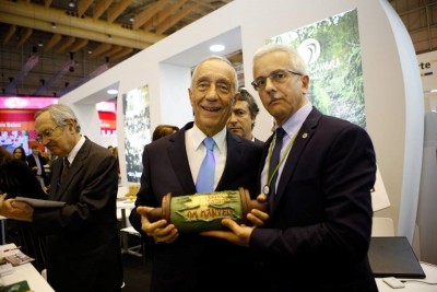 Dois homens de fato segurando objeto de madeira com rótulo Banana numa feira.