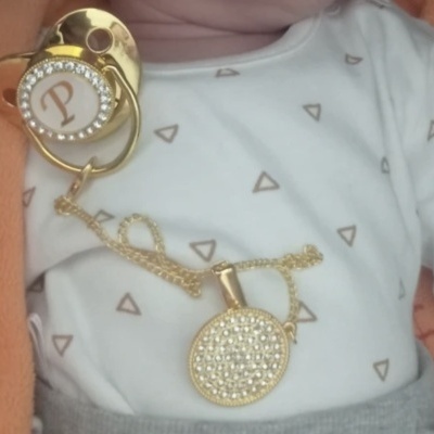 Chupeta dourada com brilhantes e letra P em roupa de bebé com padrão de triângulos