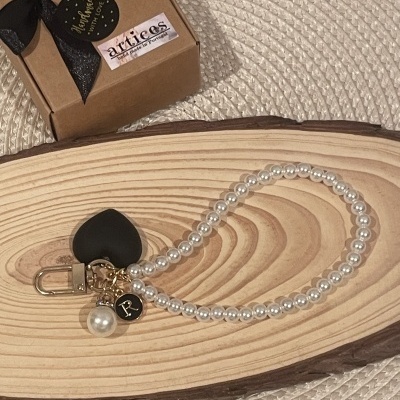 Pulseira de pérolas com pendentes preta e pérola sobre base de madeira, caixa castanha ao fundo