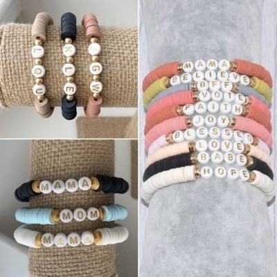 Pulseiras de missangas coloridas com letras formando palavras em português e inglês sobre tecidos bege e cinza.