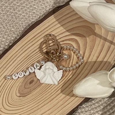 Chaveiro branco com contas, anjo e pérolas sobre madeira clara