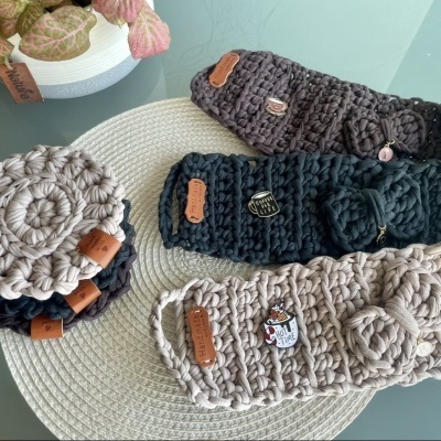 Três pares de pantufas de malha com etiquetas e pingentes sobre tapete redondo, junto a vaso com planta