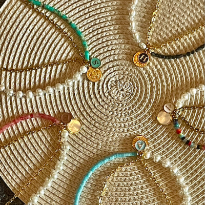 Cinco pulseiras com pérolas e contas coloridas dispostas em círculo sobre superfície de palha