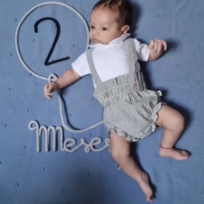 Bebé vestido com roupa às riscas sobre manta azul com texto em corda '2 Meses'.