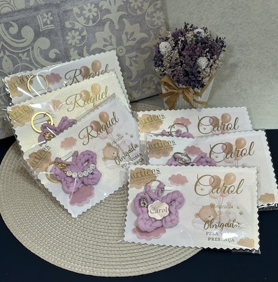 Lembranças personalizadas em cartão branco com porta-chaves roxos e arranjo de flores secas roxas e brancas