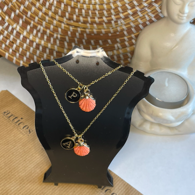 Colares dourados com pendentes concha e medalhas em busto preto com estátua branca ao lado