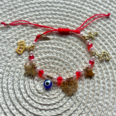 Pulseira vermelha com contas e pendentes dourados sobre fundo branco de tecido com padrão circular