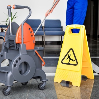 Carrinho de limpeza e sinal de aviso de piso molhado junto a pessoa a limpar chão