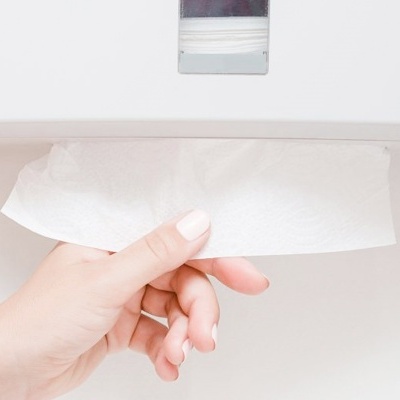 Mão feminina a puxar lenço de papel de dispensador branco na parede