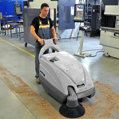 Varredora industrial cinza e preta a limpar chão de fábrica com homem a operá-la