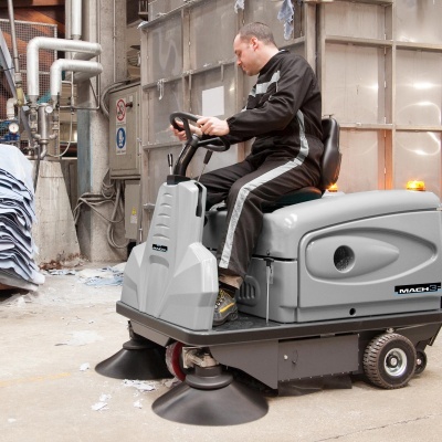 Máquina de limpeza industrial cinzenta com homem a operar em ambiente industrial