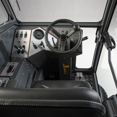 Interior de cabina de veículo industrial com volante, painel e assento preto.