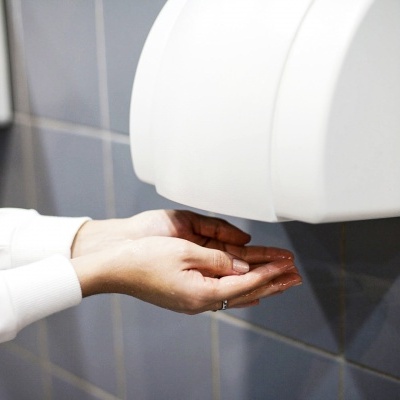 Dispenser automático branco de secador de mãos com mãos em baixo nas azulejos cinzentos