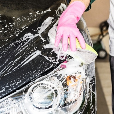 Pessoa a lavar carro preto com luvas rosas e espuma branca no farol