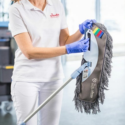 Mopa Vileda cinzenta com franjas escuras segurada por pessoa em uniforme branco com logo Vileda