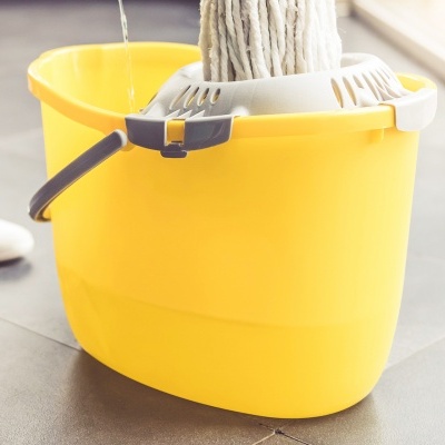 Balde amarelo de plástico com esfregona dentro, em chão cinza.