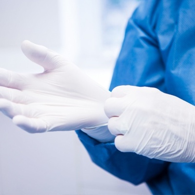 Luvas descartáveis brancas sendo colocadas numa mão por pessoa com bata azul