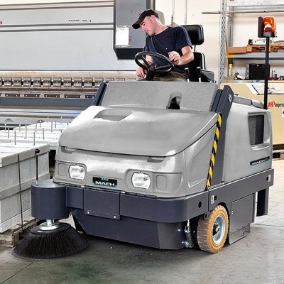 Varredora industrial cinza e preta com escova redonda operada por homem com boné preto